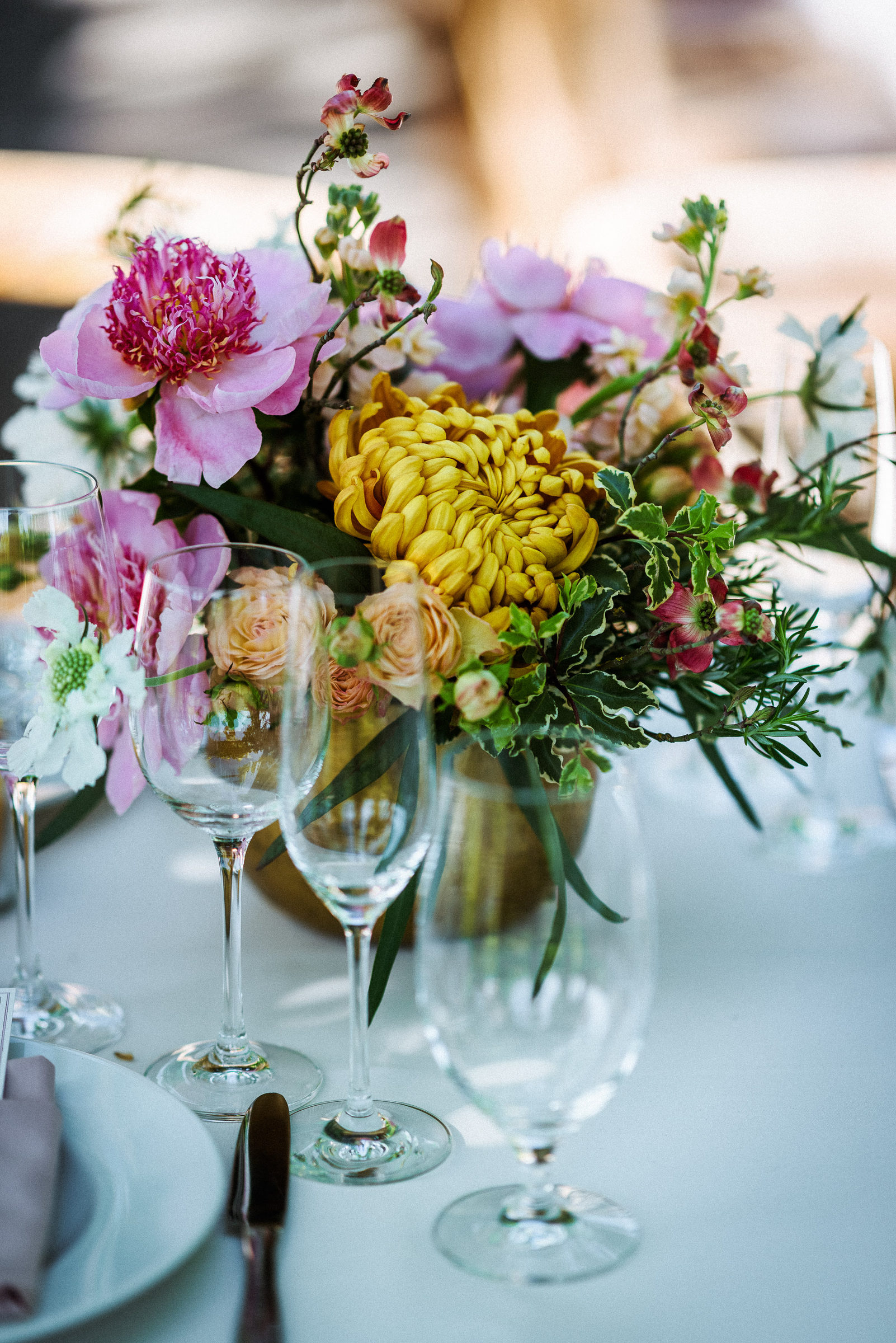 Peony and chrysanthemum centerpiece beside crystal glassware