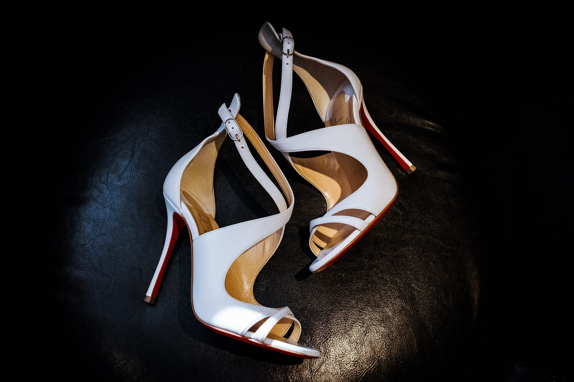 White bridal heels with scarlet soles resting on dark leather