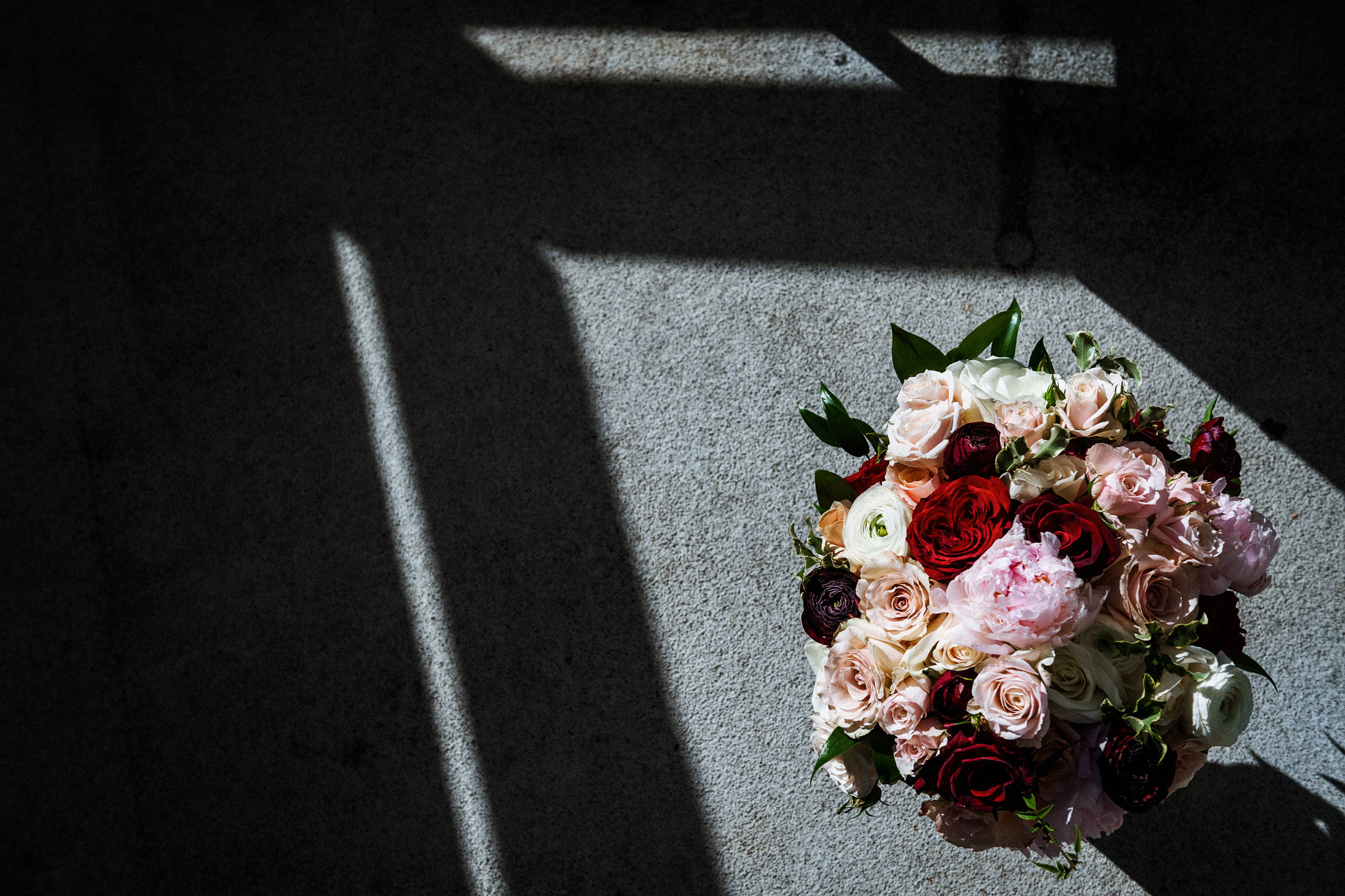 Bridal bouquet of blush and burgundy roses lit by a shaft of window light