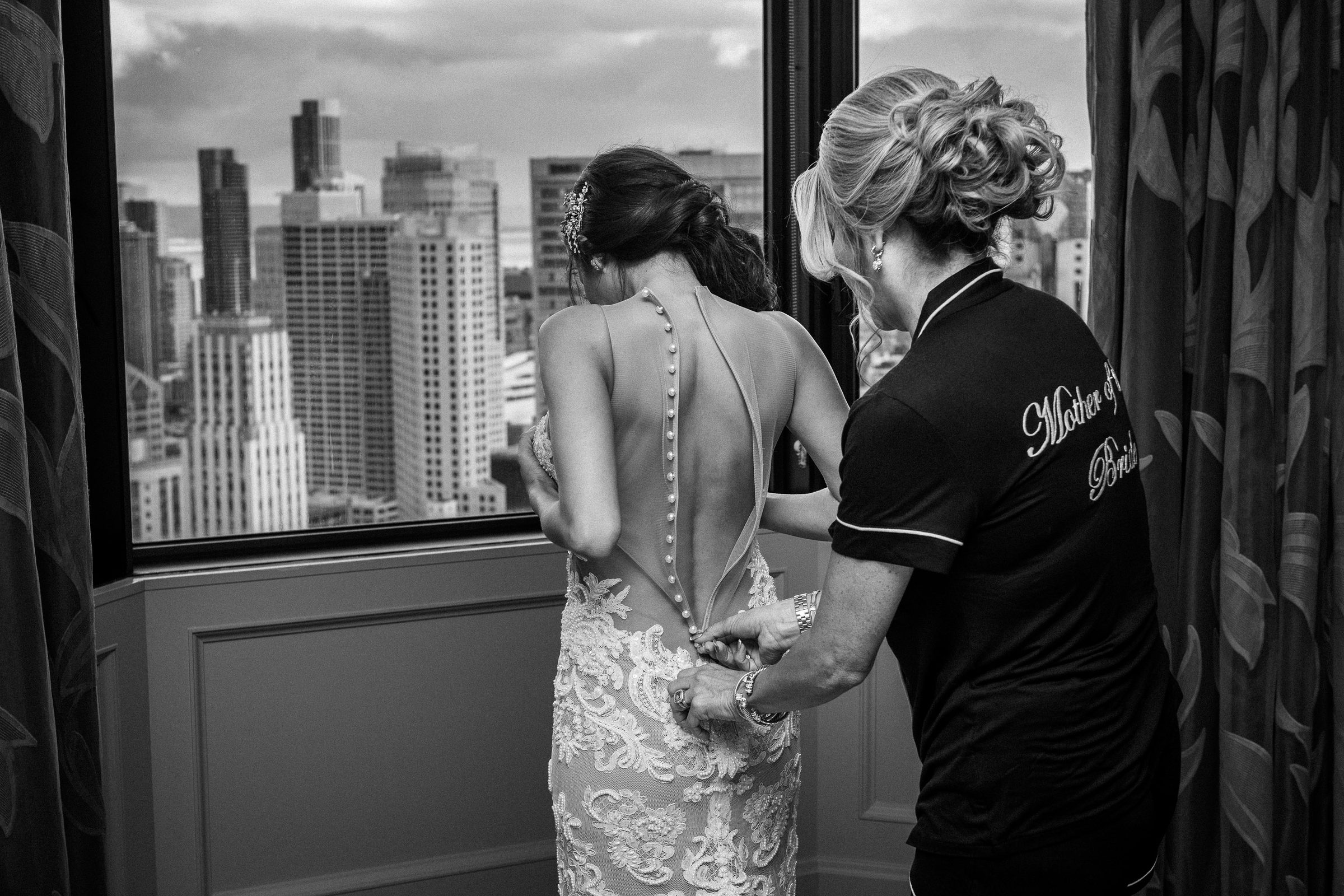 Black-and-white portrait of the mother of the bride fastening her daughter’s gown