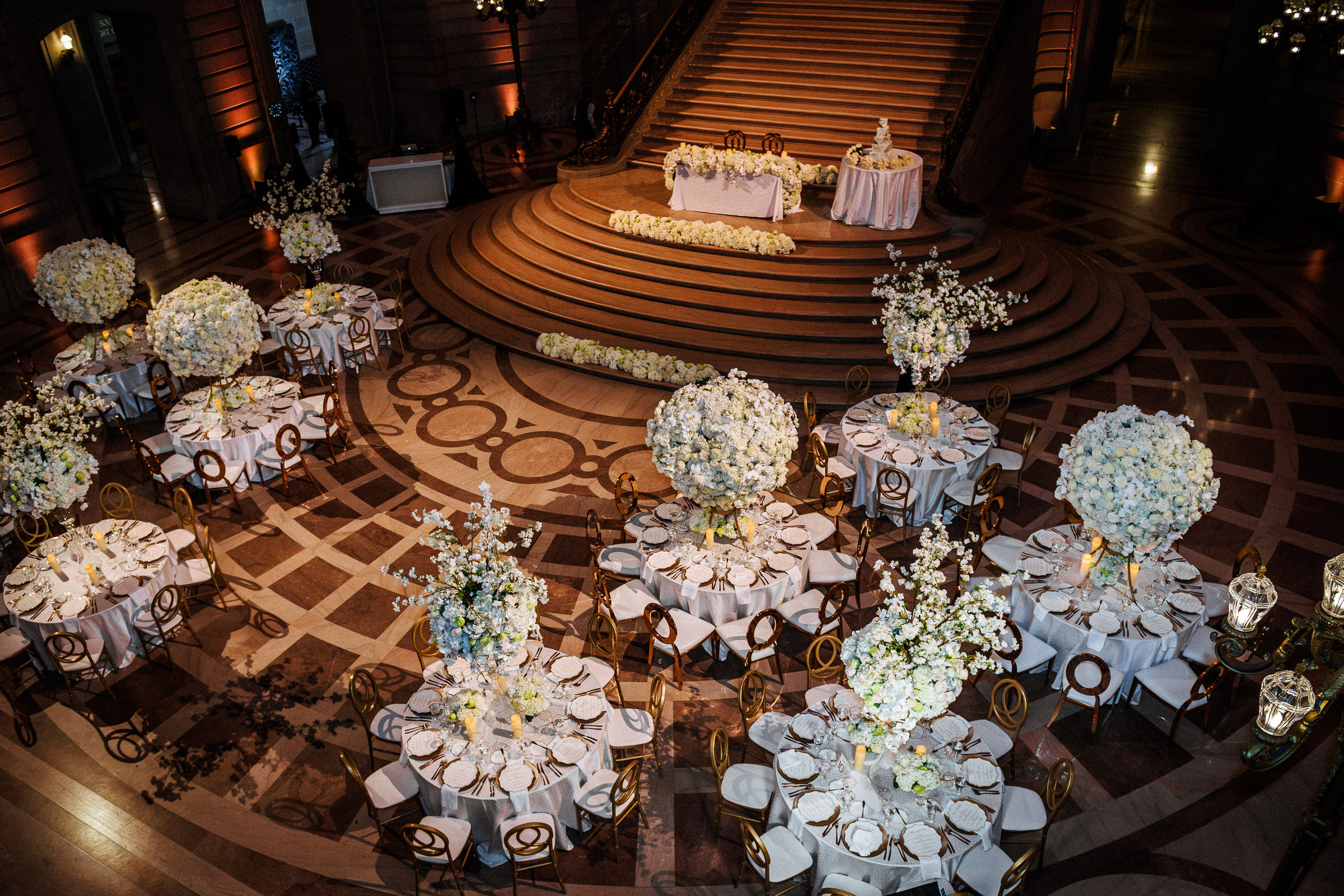 Reception tables and towering white florals set beneath the San Francisco City Hall staircase