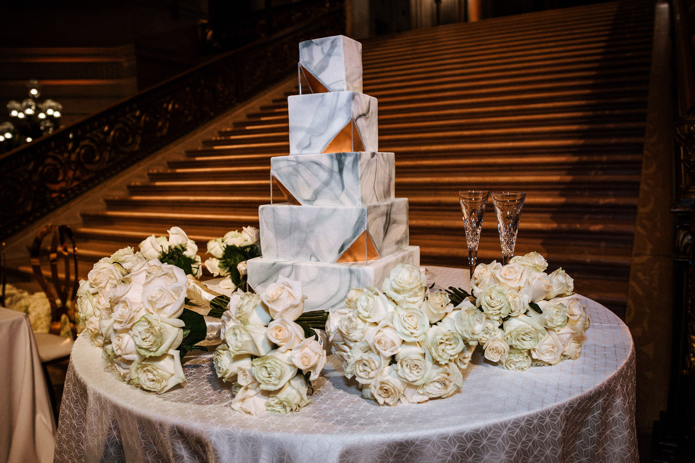 Marble-tiered wedding cake framed by bouquets of white roses