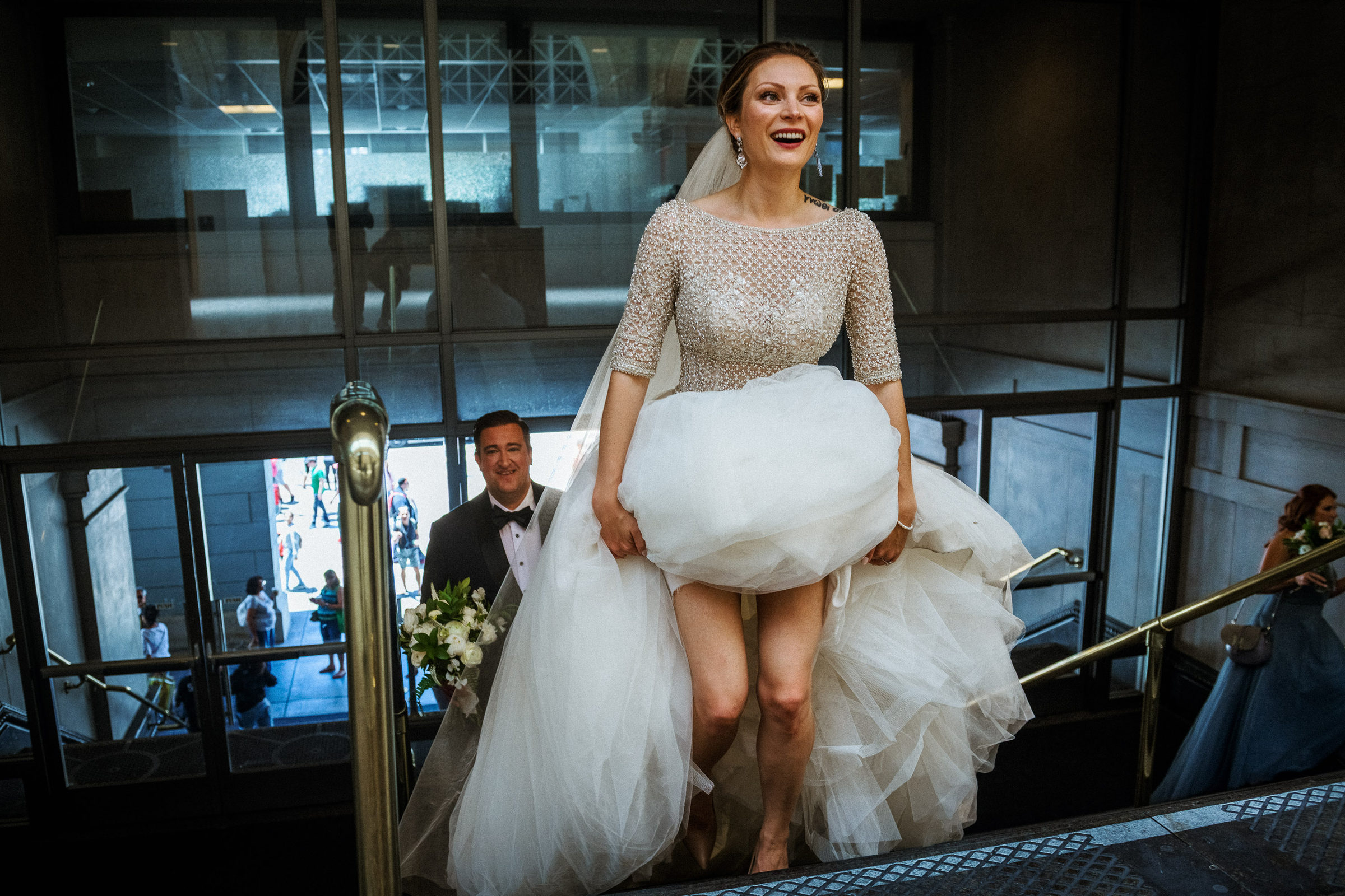Bride laughing as she lifts her gown up a downtown San Francisco stairway
