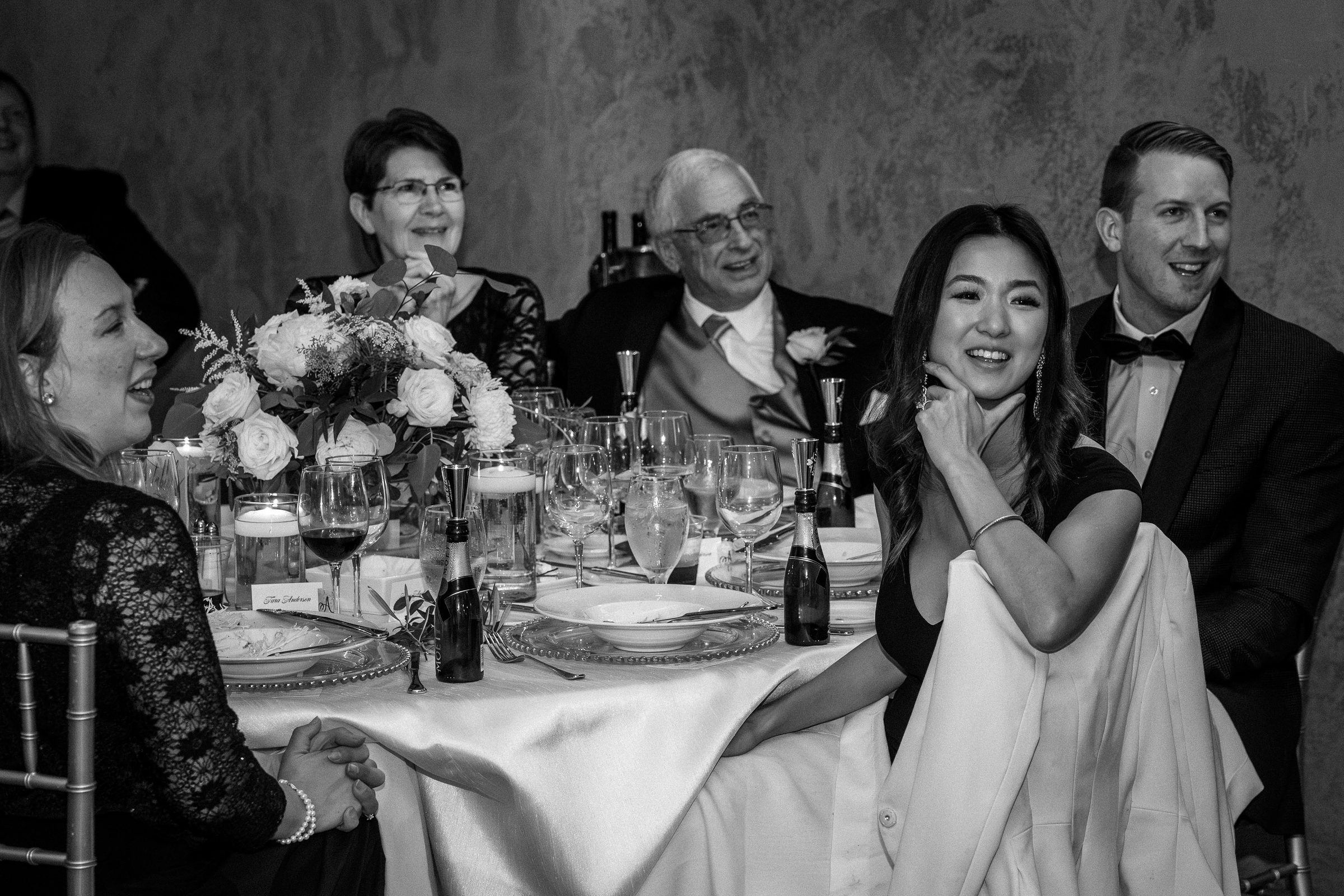 Black-and-white view of guests laughing during the wedding toasts