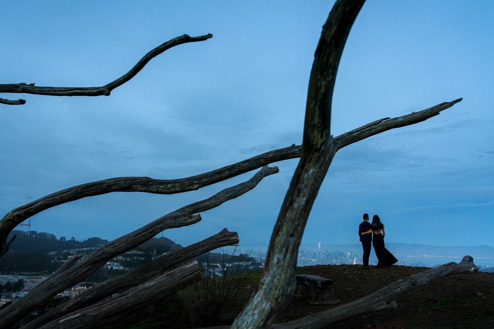 Engaged couple silhouetted on a hillside overlooking San Francisco at dusk