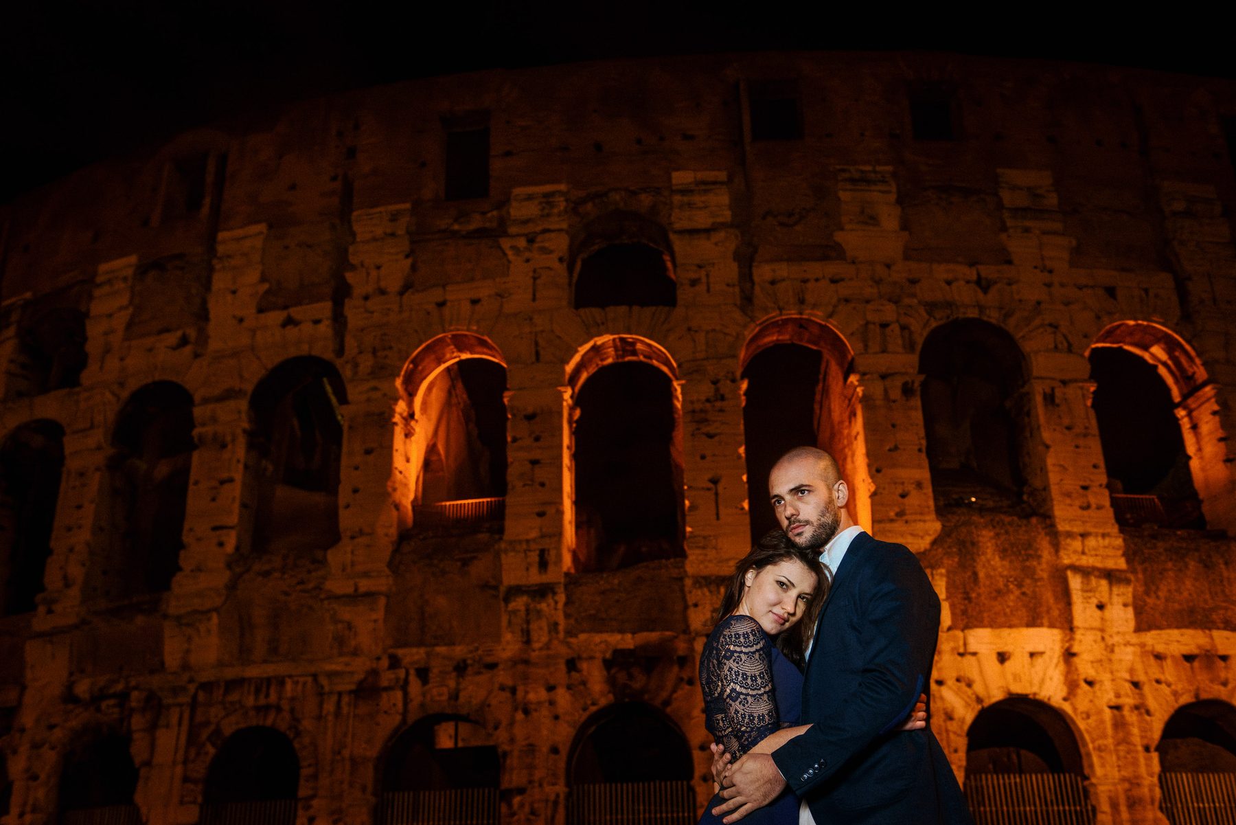 Engaged couple embracing outside the Colosseum at night in Rome