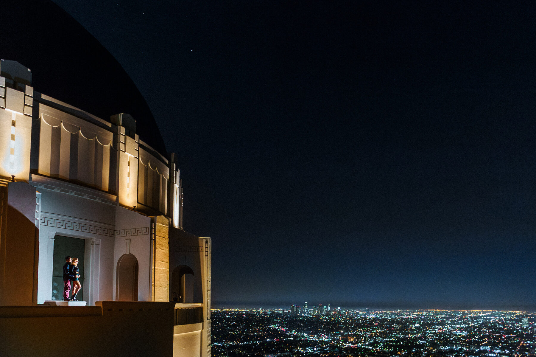 Engaged couple overlooking Los Angeles from Griffith Observatory at night