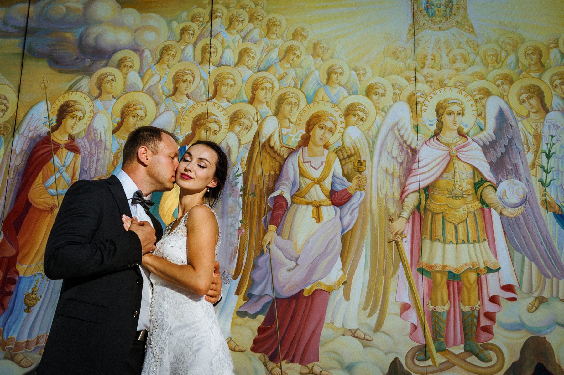 Bride and groom beside colorful angel frescoes during their Kyiv wedding portraits